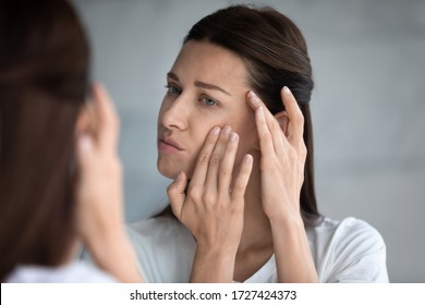 Close up reflection 35s woman touches face skin looks at mirror feeling worried about first wrinkles and age-related changes derma problems. Cosmetic facial plastic surgery skincare treatments concept - Powered by Shutterstock