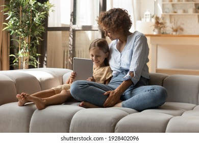 Close Relationship. Affectionate Young Mother Embrace Little Girl Sit On Sofa Use Pad Shopping At Web. Happy Family Of Two Single Mom And Daughter Kid Relax At Home Together Chat Check Social Networks