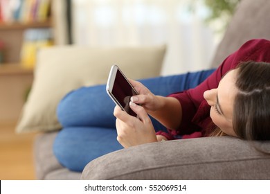 Close Up Of A Relaxed Girl Using A Smart Phone Lying On A Sofa In The Living Room At Home With A Cozy Background