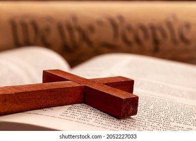 Close up of a religious cross atop the pages of a bible with the constitution in the background. 