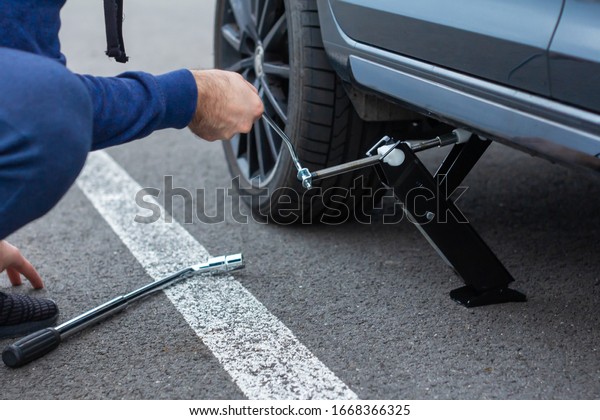 Close up of\
repair of a flat tire. Man lifts up a car using a jack for wheel\
replacement. Replacing winter and summer tires. Seasonal tire\
replacement concept. Prague, March,\
2020.