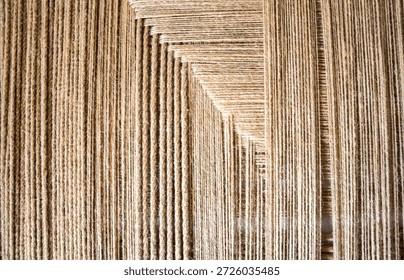 Close up reveals a complex texture of light brown twine or jute string. The fibers are arranged in tight vertical lines and layered into a geometric, triangular pattern. Texture or background