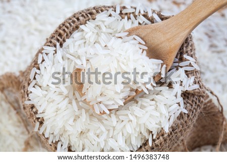 Close up the rice on wood spoon put on the rice sack with blurry of pile rice