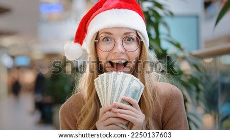 Close up rich Caucasian happy success woman lady in red Santa Christmas hat cap and eyeglass holding money dollars cash credit financial prize winning reward victory loan win finance gift to New year