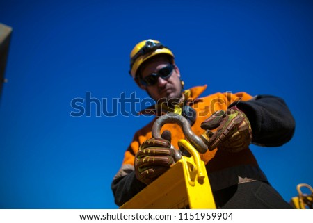 Close up rigger high risk worker wearing heavy duty glove, safety helmet fastening pin into D- shape shackle industry crane lifting lug gate at construction site Perth city, Australia 