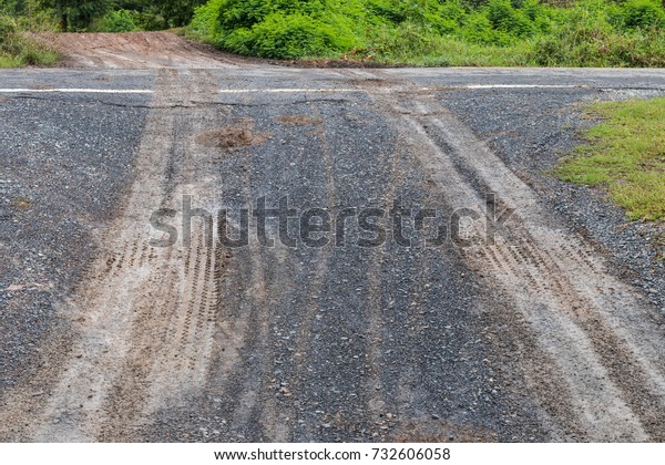 Close road surface gravel ground\
is wet from rain and traces wheel cars roaming the\
countryside.