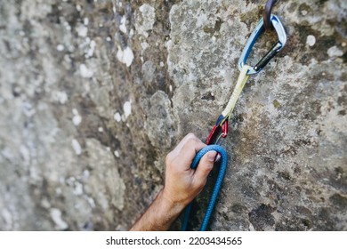 Close up of rock climber hand clipping rope in a quick draw caribener on a cliff face