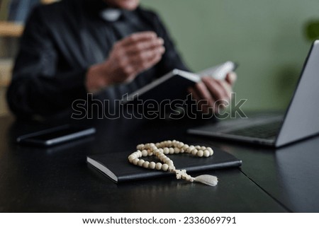 Close up of rosary on workplace desk with unrecognizable priest in background, copy space