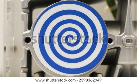 Close up of rotating white flat circle with bright blue spiral that creating hypnotic effect. HDR. Unusual robot with automated spinning hypnotic circle.