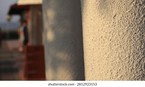 Close up of a rough beige wall texture in the foreground with a soft blurred background showing a distant figure and doorway