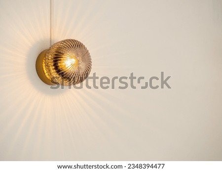 Close up round shape crystal light hanging on white wall in the interior room in cafe with copy space, minimal style. Small vintage crystal glass mounted wall lamp with refracting warm yellow light.