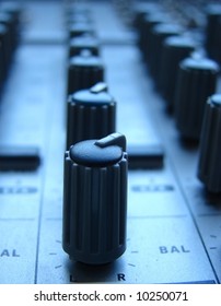 A close up of a row of mixer knobs in a blue nightly light.
