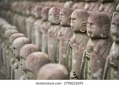 Close up of rows of small smiling stone Jizo statues at Hase-dera Temple in Kamakura