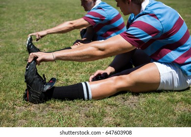 Close up of rugby players stretching while sitting on grassy field  - Powered by Shutterstock