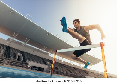 Close up of a runner jumping over an hurdle during track and field event. Athlete running a hurdle race in a stadium. - Shutterstock ID 1031588215