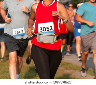 Close Up Of Runners Racing A 5K In A Trail With A Women Wearing A Fanny Pack Around Her Waist To Carry Her Personal Iteams.