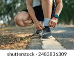 Close up - Running shoes runner man tying laces for summer run in forest park. Jogging girl exercise motivation health and fitness exercise.