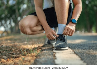 Close up - Running shoes runner man tying laces for summer run in forest park. Jogging girl exercise motivation health and fitness exercise.