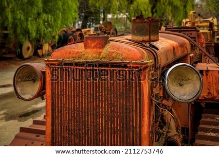 Close up of a rusted front grille and headlights of an old abandoned heavy equipment, a tractor amongst trees in a rural setting