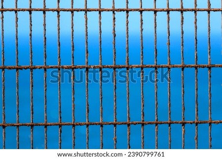 Close up of a rusted metal fence against a blue sky. Rusted metal bars in a grid pattern set against a clear, bright blue sky
