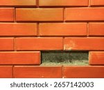 Close up of a rustic orange brick wall with a missing brick, revealing a dark recess. Ideal for themes of damage, renovation, or unique architectural textures.