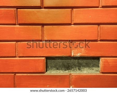 Close up of a rustic orange brick wall with a missing brick, revealing a dark recess. Ideal for themes of damage, renovation, or unique architectural textures.