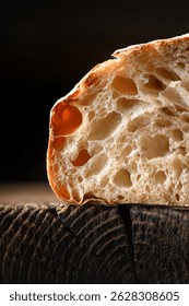 Close up of rustic sourdough bread in section with porous bread crumb and crisp skin on rustic wooden board. Macro shot of artisan loaf texture
