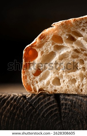 Close up of rustic sourdough bread in section with porous bread crumb and crisp skin on rustic wooden board. Macro shot of artisan loaf texture