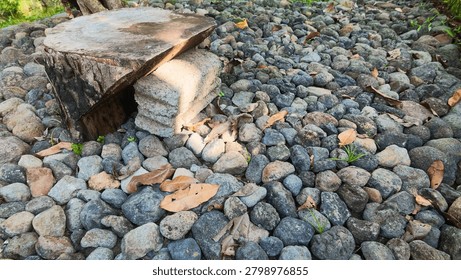 Close up of a rustic stone garden path featuring a handmade wooden log bench supported by concrete blocks