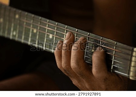 Close up of a rustic, weathered hand pressing strings on the fretboard of an acoustic guitar