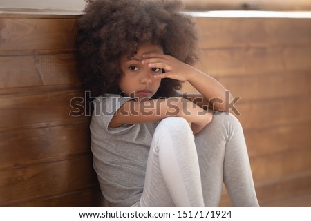 Close up sad african girl seated on floor feels lonely, mixed-race kid lost in sad thoughts need psychological support help of counsellor, racial discrimination no friends, developmental delay concept