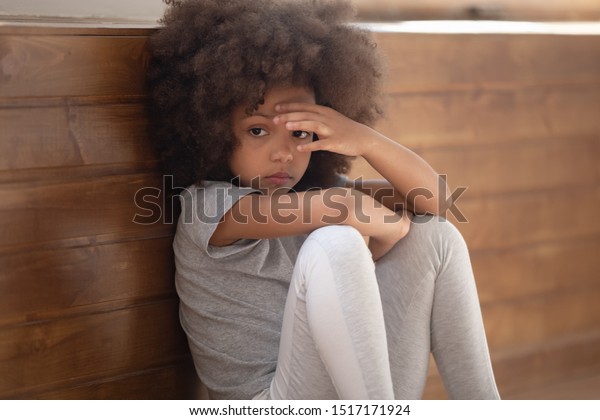 Close up sad african girl seated on floor feels\
lonely, mixed-race kid lost in sad thoughts need psychological\
support help of counsellor, racial discrimination no friends,\
developmental delay\
concept