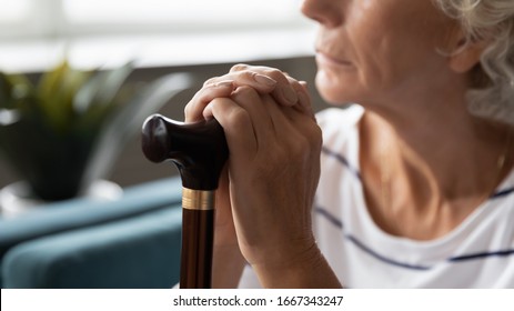 Close Up Of Sad Lonely Old Lady With Walking Stick Lost In Thoughts Thinking And Pondering At Home, Upset Abandoned Middle-aged 60s Woman With Cane Feel Distressed, Elderly Solitude Concept