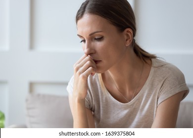 Close up of sad pensive millennial woman sit alone thinking about relationships personal problems, upset thoughtful young female lost in thoughts feel lonely depressed pondering or mourning at home