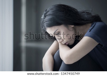 Close up of a sad woman suffering anorexia while sitting in the black background 