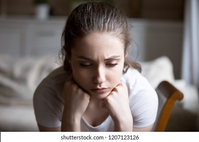 Close up sad woman thinking sitting alone at home. Portrait millennial female feels unhappy and depressed, has a problem in relationships broken heart after break up or quarrel with boyfriend concept