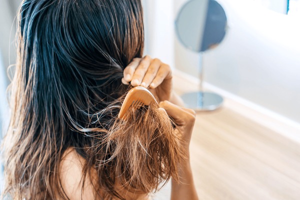 Close up of sad young Asian woman brush her damaged and tangled wet hair.