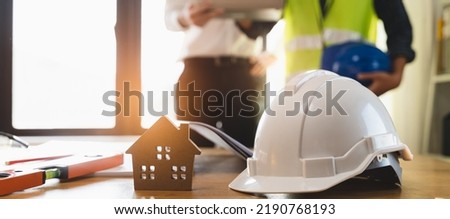 Close up safety helmet on the table and contractor and customer shaking hands after confirm to build home.