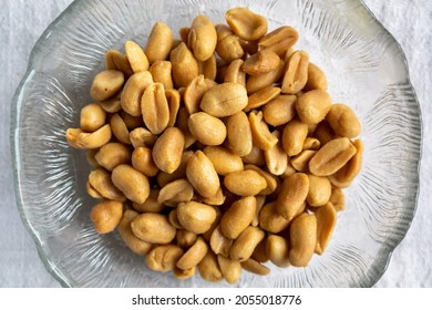 Close Up Of Salted Peanuts In A Glass Bowl. Overhead View With White Background