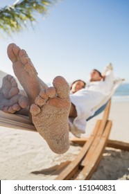 Close Up Of Sandy Feet Of Couple Sleeping In A Hammock On The Beach