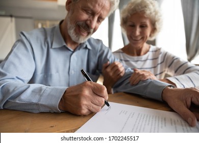 Close Up Satisfied Older Couple Signing Documents, Making Purchasing Or Investment Deal, Smiling Mature Husband And Wife Holding Hands, Putting Signature On Contract, Buying House Or Taking Loan