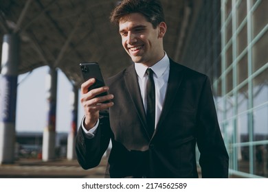 Close up satisfied young traveler businessman man in black suit standing outside at international airport terminal use mobile cell phone book taxi order hotel online Air flight business trip concept.
