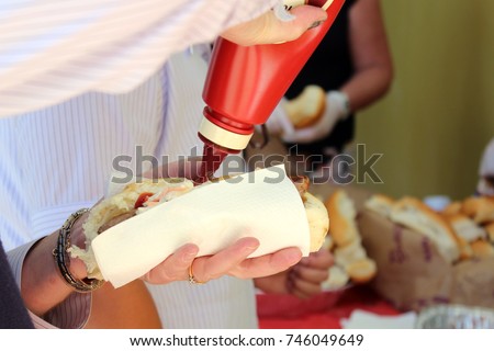 Close up of sausage in a roll, with sauce being added, at a sausage sizzle