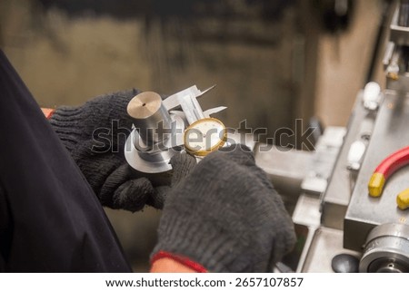Close up scene the machine operator measuring dimension of metal shaft parts by dial Vernier caliper. The parts quality control by vernier caliper on turning machine by machine operator.
