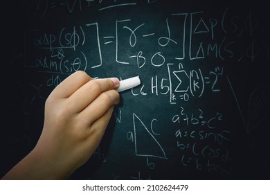 Close up of schoolgirl hand writing mathematics formula on the blackboard while studying in the classroom - Powered by Shutterstock