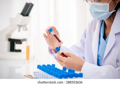 Close Up Of Scientist Holding And Examining Blood Sample In Lab
