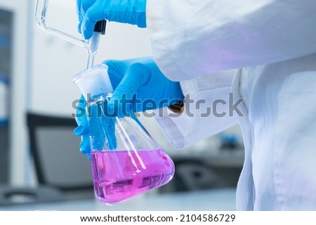 Close up scientist uses a titration method of analysis to study the chemical properties of the water sample. Scientist holding Erlenmeyer flask with pink solution