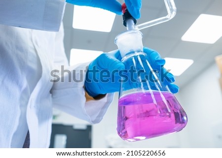 Close up scientist uses a titration method of analysis to study the chemical properties of the water sample. Scientist holding Erlenmeyer flask with pink solution