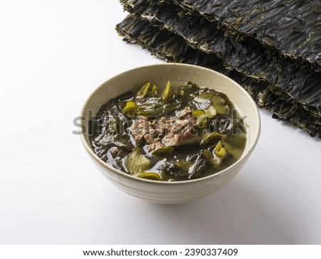 Close up of sea mustard soup with beef on ceramic bowl with stacked dried sea mustard on white floor, South Korea
