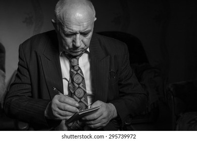 Close up Seated Old Bald Businessman Writing Some Notes on his Small Notebook with Serious Facial Expression in Monochrome Color.